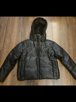Zara svart vattentät pufferjacka – varm , XS/S - Svart pufferjacka från Zara. Vattentät jacka med isolering ner till ca -10°C – perfekt för kalla och blöta vinterdagar. Snygg modell i syntetmaterial med skinnlook som passar till allt. Jackan har huva, dragkedja framtill och dragsko nedtill för bättre passform. Oversized modell som passar både S. Säljs då den inte längre används. Redo att användas direkt.