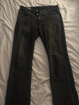 Svarta raka jeans från Levi's - Säljer ett par svarta jeans från Levi's med klassisk rak passform. Jeansen har knappgylf och detaljer i metall.