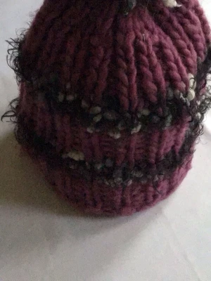 Lila stickad mössa med tofs - Säljer en chunky stickad mössa i lila med svarta och vita inslag samt en liten tofs på toppen. Mössan har bred ribbstickning och är gjord i tjockt garn, perfekt för kalla dagar. Passar dig som gillar en unik och mysig stil.