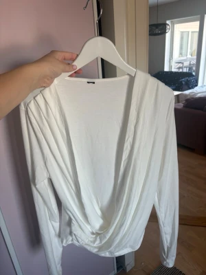 Vit omlottopp med lång ärm ☁️☁️ - Snygg vit omlottopp med djup v-ringning och långa ärmar. Toppen har ett draperat omlottparti framtill som ger en cool och avslappnad look. Perfekt att styla med jeans eller kjol för en trendig outfit. Massage L/M