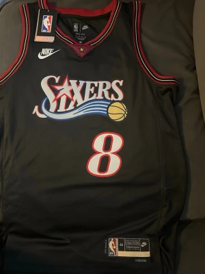 76Sixers basketlinne, classic edition Paul George #8 - Säljer ett svart basketlinne från Nike med Philadelphia 76ers-logga och nummer 8 på framsidan. Linnet har röda och vita detaljer samt broderad NBA-logga. Tillverkat i meshmaterial som andas, perfekt för basket eller träning.