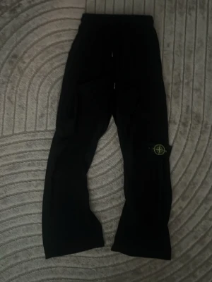 Stonę lsland  svarta byxor - Svarta nylon byxor från Stone Island med klassisk logotyp-patch på benet. Byxorna har avslappnad passform och dragsko i midjan. Perfekta för en chill och trendig look. Materialet känns mjukt och bekvämt mot huden. 