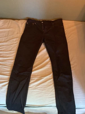 Svarta jeans från Levi's - Säljer ett par svarta jeans från Levi's med klassisk femficksmodell och raka ben. Jeansen har en diskret röd Levi's-tag på bakfickan och är tillverkade i ett slitstarkt denimtyg. Perfekta för dig som gillar en tidlös och clean look. Kontakta vid fler frågor!