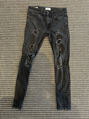 Svarta ripped jeans från Only & Sons - Säljer ett par svarta skinny jeans från Only & Sons med flera slitningar och hål på benen för en riktigt edgy look. Jeansen har klassisk femficksmodell och knappgylf. Perfekta för dig som gillar streetstyle och vill sticka ut.