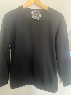 Svart sweatshirt från Stone Island - Snygg svart sweatshirt från Stone Island med klassisk rund hals och lång ärm. Tröjan har den ikoniska loggan på vänster ärm och är tillverkad i mjukt bomullsmaterial. Perfekt för en clean och stilren look.