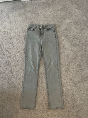 Ljusgrå raka jeans - Säljer ett par ljusgrå jeans med rak passform och klassisk femficksdesign. Jeansen har bälteshällor, knappgylf och är tillverkade i ett mjukt denimtyg. Perfekta för en clean och stilren look.