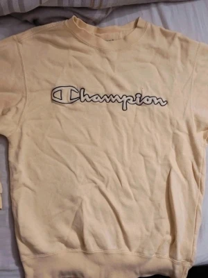 Gul sweatshirt från Champion - Säljer en ljusgul sweatshirt från Champion med det klassiska broderade logotypen framtill. Tröjan har rund halsringning, långa ärmar och ribbade muddar vid ärmslut och nederkant. Perfekt för en avslappnad och sportig stil.