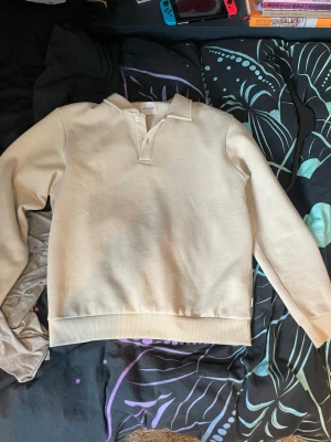 Beige collagetröja med knappar - Snygg beige collagetröja med krage och två knappar vid halsen. Tröjan har långa ärmar och breda muddar vid ärmslut och nederkant. Perfekt för en avslappnad och stilren look. Priset är inte huggit i sten och tar gröna emot prisförslag.