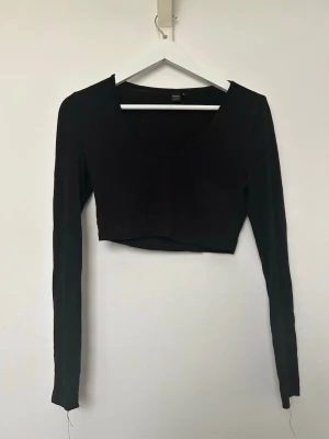 Svart croppad långärmad topp - En svart croppad topp med lång ärm och rundad halsringning. Enkel och stilren design som passar perfekt till höga jeans eller kjol. Tillverkad i mjukt material för en bekväm känsla. Använd fåtalet gånger men i fint skick. Storlek S. 