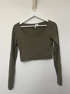 Olivgrön Croppad ribbad topp - H&M - Trendig olivgrön croppad topp från H&M med lång ärm och rund halsringning. Tillverkad i ribbad bomullsmix som ger en skön och stretchig passform. Använd men i fint skick. Storlek S. 