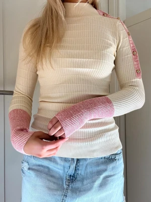 Max Mara krämvit ribbad tröja med rosa detaljer - Trendig ribbstickad tröja i krämvitt med rosa muddar och axelparti. Guldknappar längs ena axeln ger en snygg detalj. Hög hals och lång ärm. Perfekt till jeans eller kjol i sommar💗💗Från Max Mara med originalpris runt 1500 kr. Mycket bra skick. 
