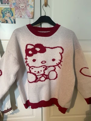 Hello Kitty stickad tröja röd/vit - Supersöt stickad tröja med stor Hello Kitty och nalle i rött på framsidan. Tröjan är vit med röda detaljer vid hals, ärmslut och nederkant samt ett hjärta på ärmen. Oversized passform och rund halsringning. Köpt på Aliexpress 2023 för 225kr. Knappt använd utan defekter. Oversized M-L. Skicka PM för bevis av kvitto.