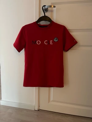 Röd Moncler t-shirt med logga - Snygg röd t-shirt från Moncler med korta ärmar och tryckt logga samt text på bröstet. Klassisk rak passform och rund halsringning. Perfekt för dig som vill ha en stilren och trendig look.