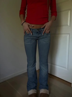 Ljusblå bootcut jeans låg midja - Säljer ett par ljusblå bootcut jeans med låg midja och klassiska fem fickor. Jeansen har en lätt tvättad look och är tillverkade i denim med lite stretch för skön passform. Perfekta till sneakers eller boots.