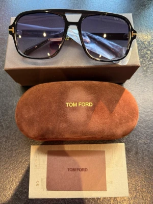 Tom Ford Falconer-02 FT0884 – Nya med prislapp | Nypris 3 739 kr - Sälj ett par exklusiva och stilrena Tom Ford Falconer-02 (FT0884) solglasögon i klassisk pilotmodell. Den blanksvarta acetatbågen kombineras elegant med Tom Fords ikoniska guldfärgade T-detaljer på skalmarna, vilket ger en tidlös och lyxig look.  Helt nya – aldrig använda Prislapp kvar Originalpris: 3 739 kr Klassisk pilotdesign som passar både dam och herr Exklusiv känsla och hög kvalitet från Tom Ford  