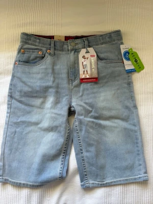 Levi's ljusblå jeansshorts slim fit - Snygga ljusblå jeansshorts från Levi's i slim fit-modell. Klassisk femficksdesign, bälteshällor och knappgylf. Tillverkade i bomull med en skön och avslappnad känsla. Perfekta för sommaren och enkel att matcha med olika stilar.