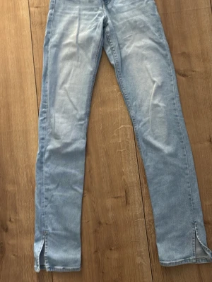 Ljusblå raka jeans med slits - Säljer ett par ljusblå jeans i rak modell med slitsar längst ner vid bensluten. Jeansen har klassisk femficksdesign och är gjorda i denim. Perfekta för dig som gillar en avslappnad och trendig look.