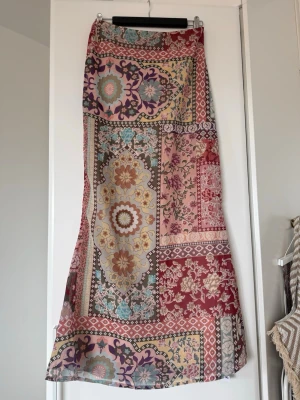 Mönstrad långkjol i boho-stil från Boohoo  - Säljer en färgglad långkjol med patchworkmönster i rött, rosa, beige och blått. Kjolen har blommiga och geometriska detaljer och är gjord i ett lätt, flödande material som passar perfekt till sommaren. Ingen stretch i midjan och utan synliga fickor.
