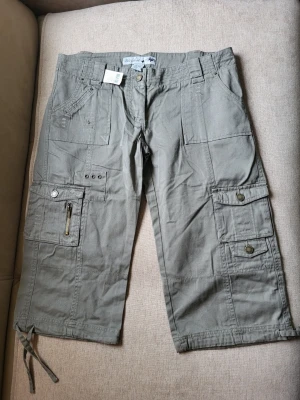 Khaki cargobyxor med fickor Wet Seal Storlek 7US M - Stilrena khaki cargobyxor med flera stora fickor, dragkedjedetalj och knappar. Byxorna har snörning vid benslut och är tillverkade i ett slitstarkt bomullstyg. Perfekta för en avslappnad streetstil.