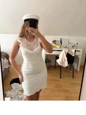Studentklänning vit spetsklänning  - Säljer en superfin vit kort spetsklänning med volangdetaljer vid axlarna och transparent mesh upptill. Klänningen har figurnära passform och v-ringad illusion vid halsen. Perfekt till student eller sommarens alla tillfällen! Användes aldrig till studenten köpte en annan.