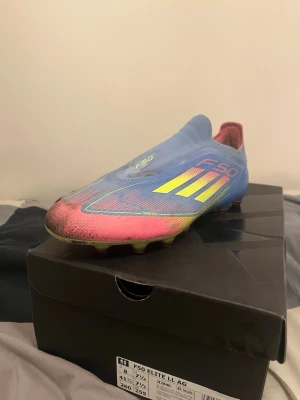 Adidas F50 Elite LL AG fotbollsskor - Säljer ett par Adidas F50 Elite LL AG fotbollsskor i blått, gult och rosa. Skorna har en strömlinjeformad design utan snörning och är tillverkade i syntetmaterial. Sulan har fasta dobbar för konstgräs och coola färgövergångar. Skriv om du har frågor!