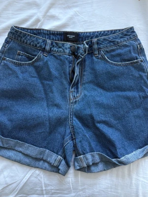 Blå denimshorts från Vero Moda - Klassiska blå denimshorts från Vero Moda med hög midja och uppvikta benslut. Perfekta för sommaren och enkla att matcha med olika stilar.