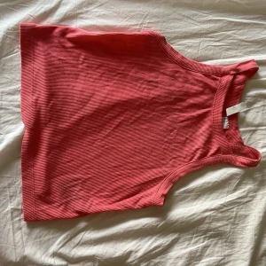 Rosa ribbad linnetopp - Säljer en snygg rosa ribbad linnetopp med breda axelband och rundad halsringning. Toppen är croppad och har en enkel, stilren design som passar perfekt till jeans eller kjol. Materialet är mjukt och stretchigt för en bekväm passform.