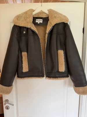 Brun jacka från NA-KD - Säljer en brun jacka från NA-KD med beige fuskpäls på insidan. Använd enstaka gånger men inget som märks, den är i väldigt bra skick! Nypris 1299 kr