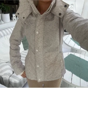 Ljusgrå  Hollister jacka XS - Snygg ljusgrå allvädersjacka från Hollister med hög krage och tryckknappar framtill. Jackan har en sportig look och är tillverkad i mjukt syntetmaterial med fleecefoder för extra komfort. Perfekt för kyliga dagar. 