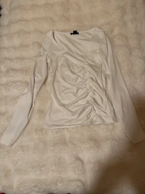 Vit långärmad topp från Amisu på new yorker - Säljer en vit långärmad topp från Amisu med snygg rynkning på framsidan. Toppen har en figurnära passform och är tillverkad i ett mjukt, stretchigt material som känns skönt mot huden. Perfekt att styla med jeans eller kjol.