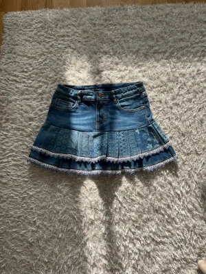 Blå jeanskjol med volang och spets - En Lågmidjad jeanskjol omsydd från ett par jeans. Stretchig  Midjemått tvärsöver: 34cm Längd: 34cm