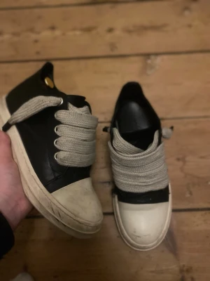 Svarta Ramones jumbo lace - Snygga svarta sneakers med breda, gråvita snören och vit sula. Skorna har en chunky look med rund tå och kontrasterande vit tåhätta. Tillverkade i slätt material som ser ut som läder. Perfekta för en streetwear-stil.