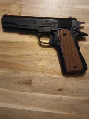 Svart luftpistol med brunt grepp - Säljer en svart luftpistol med klassisk design och brunt räfflat grepp i plast. Pistolen har detaljer i metall och tydliga markeringar på sidan. Perfekt för dig som gillar airsoft eller samlar på replikor.saknar magasin