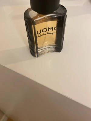 UOMO parfym från Salvatore Ferragamo - UOMO från Salvatore Ferragamo är en elegant herrparfym i en stilren, svart och transparent glasflaska med räfflade kanter. Flaskan har en maskulin design och innehåller 30 ml doft. Perfekt för dig som gillar exklusiva och moderna parfymer. 90% kvar. 