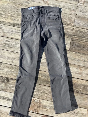 Grå jeans från replay - Säljer ett par grå jeans från Nudie Jeans med klassisk femficksmodell och raka ben. Jeansen har en diskret tvättad look och är tillverkade i mjukt bomullsmaterial. Perfekta för en avslappnad och stilren outfit. Strl 29-32