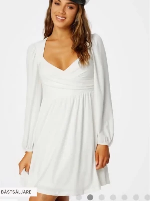 Studentklänning  / kort klänning  - Snygg vit kortklänning från Bubbleroom omlott-design och v-ringad hals. Klänningen har långa ärmar med lätt puff och elastiska muddar. Materialet är mjukt och lätt, perfekt för studenten eller som fin sommarklänning. Stilren och enkel att matcha med olika accessoarer. Klänningen är endast provade så nyskick med lappen kvar. Storlek S (36).