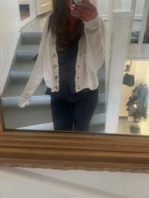 Beige Zara kofta  - Säljer en söt vit cropped kofta med dekorativa knappar framtill. Koftan har långa ärmar och en mjuk, stickad känsla som passar perfekt till jeans eller kjol. Enkel och stilren design som är lätt att matcha.