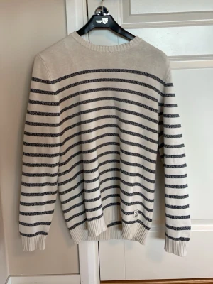 Randig stickad tröja Dobber - Snygg stickad tröja från Dobber i offwhite med mörkblå horisontella ränder. Tröjan har rund halsringning, långa ärmar och ribbade muddar vid ärmslut och nederkant. Perfekt till jeans för en avslappnad men stilren look.