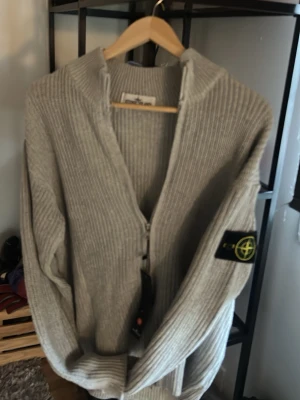 Ljusgrå stickad ziptröja Stone Island - Säljer en ljusgrå stickad ziptröja från Stone Island med ikonisk patch på ärmen. Tröjan är som en quarter zip fast med lång zip