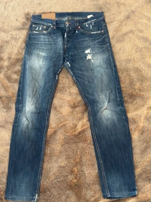Dondup jeans - Säljer ett par blå dondup jeans med slitningar och distressed detaljer på både fram- och baksida. Jeansen har raka ben, klassisk femficksmodell och kontrastsömmar. Materialet är denim i bomull och de har en cool, använd look.