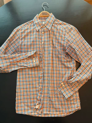 Eton skjorta - Snygg rutig skjorta från Eton i blått, orange och vitt. Skjortan har klassisk krage, långa ärmar och knäppning framtill. Tillverkad i mjuk bomull som känns skön mot huden. Perfekt för dig som gillar färg och mönster.