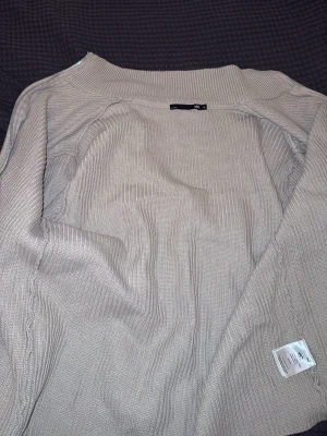 Beige stickad tröja från Gina Tricot - Snygg beige stickad tröja från Gina Tricot med rund halsringning och ribbade detaljer. Tröjan har en avslappnad passform och är perfekt för lager på lager. Materialet är mjukt och bekvämt, vilket gör den enkel att bära till olika outfits.