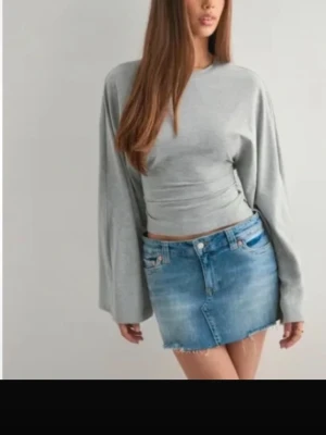 Grå långärmad topp från Nelly - Säljer en stilren grå croppad topp med långa, vida ärmar. Toppen har en enkel design och är perfekt att matcha med jeans eller kjol. Materialet känns mjukt och bekvämt, och modellen ger en avslappnad men trendig look.