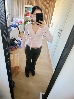 Ljusrosa omlottopp med knyt - Säljer en ljusrosa omlottopp med långa ärmar och knyt i sidan. Toppen har en djup v-ringning och är croppad i modellen. Perfekt att styla med höga jeans eller kjol för en trendig look.