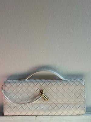 Bottega veneta styled clutch - Snygg vit kuvertväska i quiltat mönster med guldfärgad vridlåsdetalj framtill. Väskan har ett litet handtag upptill och en stilren, rektangulär form. Perfekt accessoar för att lyfta din outfit.