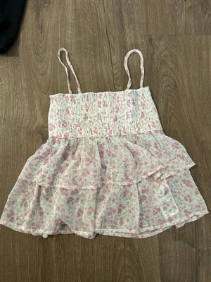 Blommig volangtop med smala axelband - Söt topp med volanger och smala axelband i ljusrosa och vitt blommigt mönster från Gina tricot i barn storlek 134/140. Toppen har smockad överdel och är tillverkad i ett lätt, luftigt material som passar perfekt till varma dagar.🩷🩷