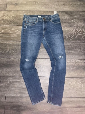 Jeans med slitningar  - Tjena! Säljer dessa feta blåa jeansen med skinny fit och slitningar på knäna 🤙. Jeansen har klassiska fickor, dragkedja och knapp framtill samt snygga detaljer med ljus tvätt. Materialet är bomullsdenim med stretch för skön passform. Skriv vid intresse eller övriga funderingar 🥂
