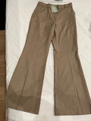 Beiga chinos med utsvängda ben - Snygga beiga chinos med utsvängda ben och normal hög midja. Byxorna har bälteshällor, snedställda fickor fram och är tillverkade i ett mjukt bomullsmaterial. Perfekta för en trendig och avslappnad stil.