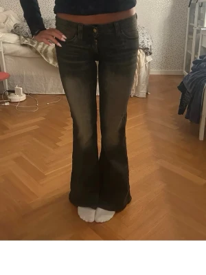 Svarta bootcut jeans med slitningar - Säljer ett par svarta bootcut jeans med lätt slitna detaljer och klassisk femficksmodell. Jeansen har hög midja, dragkedja och knapp framtill samt bälteshällor. Materialet är stretchigt denim som sitter snyggt på kroppen.