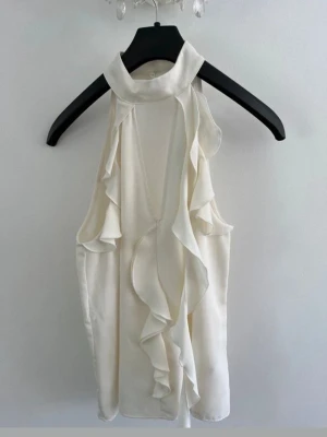 Vit ärmlös linnetopp med volang - Stilren vit linnetopp med hög hals och volangdetaljer framtill. Toppen är ärmlös.